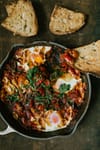 shakshuka tomato based dish in a pan with sourdough bread toasts on the side