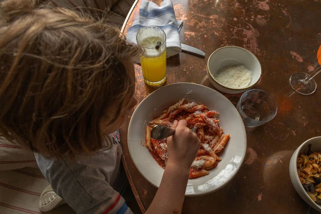 girl eating pasta with tomato sauce dish