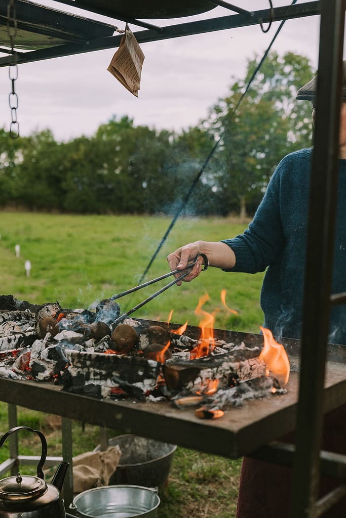 Woman using tongs to cook over open fire