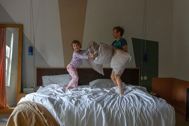 children pillow fighting on king's size bed